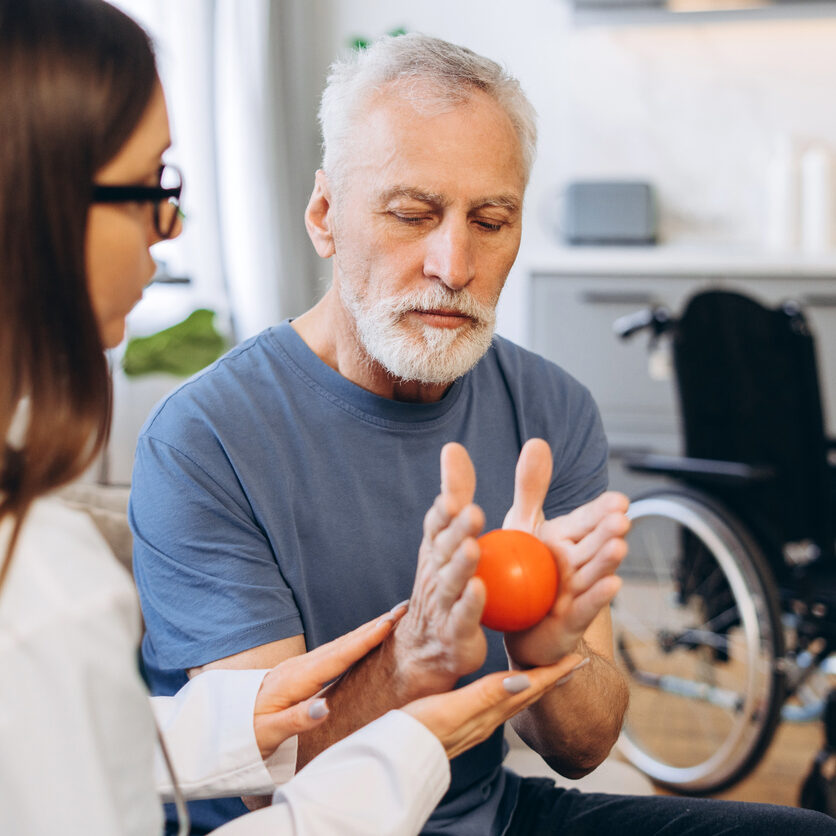 Doctor helping a mature adult man with hand exercises using a stress ball, focusing on rehabilitation and recovery
